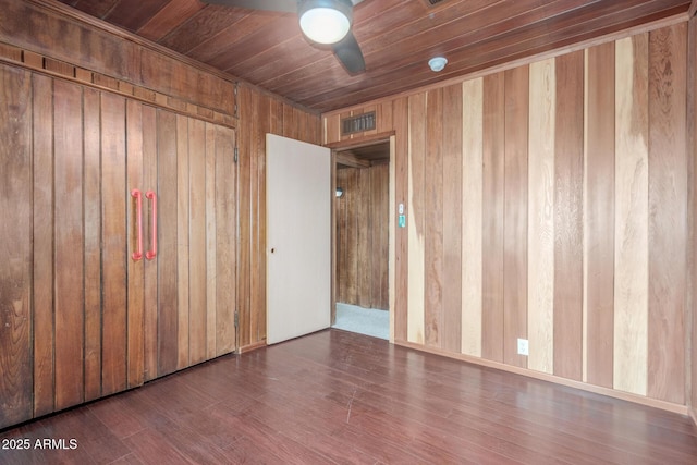 empty room featuring visible vents, ceiling fan, wooden walls, wood finished floors, and wooden ceiling