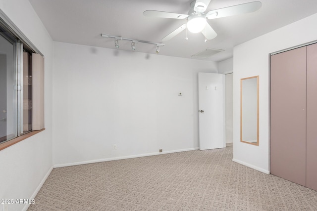 unfurnished bedroom with carpet, a closet, rail lighting, a ceiling fan, and baseboards