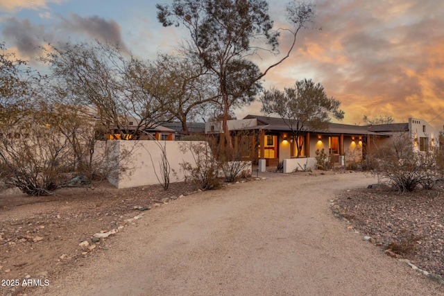 back of property at dusk with dirt driveway and fence