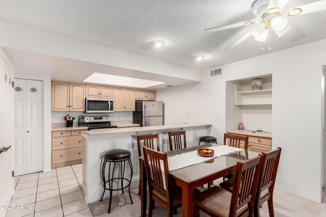 kitchen with appliances with stainless steel finishes, a breakfast bar area, light brown cabinets, and kitchen peninsula