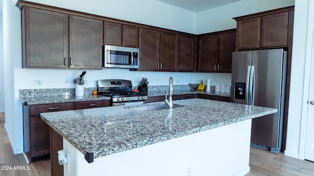 kitchen with sink, stainless steel appliances, light stone counters, light hardwood / wood-style flooring, and a center island with sink