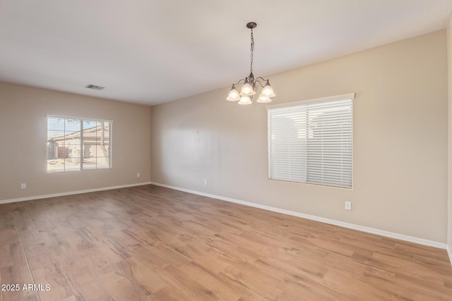 empty room featuring baseboards, light wood-type flooring, and a notable chandelier