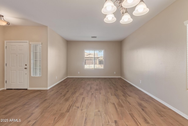 interior space featuring visible vents, light wood-style flooring, baseboards, and an inviting chandelier