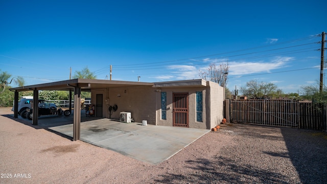 rear view of house with stucco siding, fence, a gate, and a carport