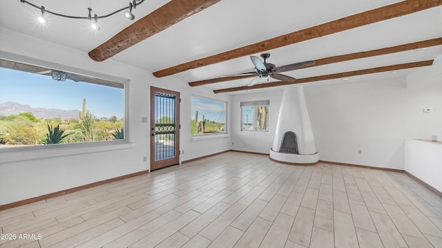 spare room with baseboards, a large fireplace, ceiling fan, and beamed ceiling