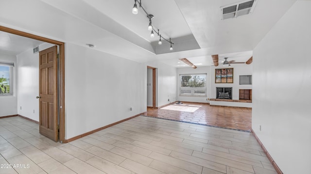 unfurnished living room with a tray ceiling, baseboards, a ceiling fan, and visible vents