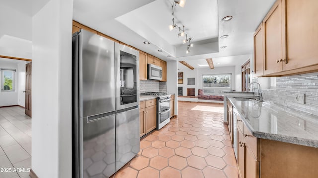 kitchen featuring light stone counters, a sink, stainless steel appliances, decorative backsplash, and light tile patterned floors