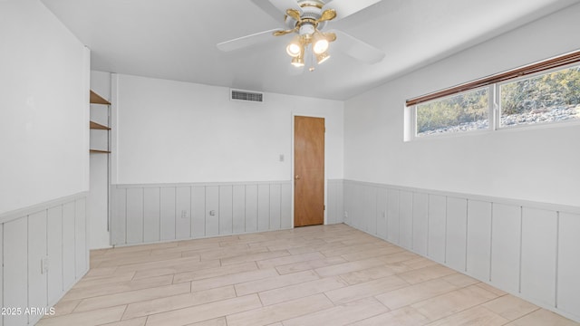 empty room featuring visible vents, a ceiling fan, wainscoting, and wood finished floors