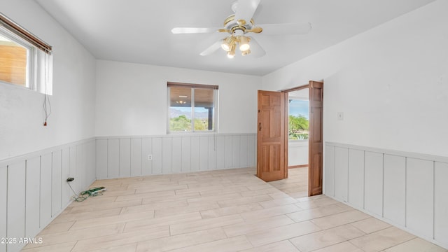 spare room with plenty of natural light, wainscoting, and ceiling fan