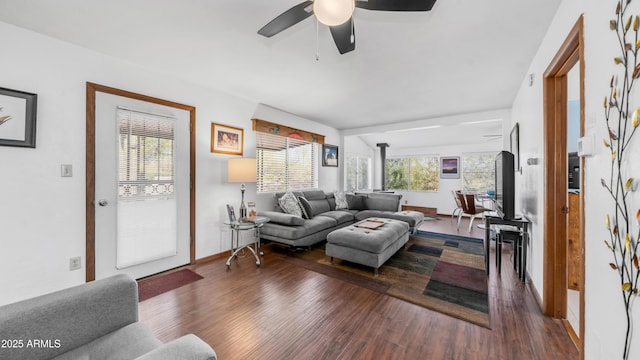 living room featuring baseboards, a ceiling fan, wood finished floors, and a wood stove
