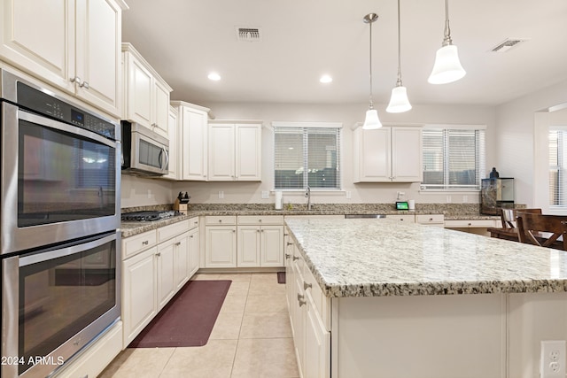 kitchen with a kitchen island, pendant lighting, white cabinetry, light tile patterned floors, and appliances with stainless steel finishes