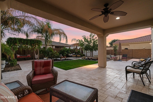 patio terrace at dusk featuring a yard, ceiling fan, and an outdoor hangout area