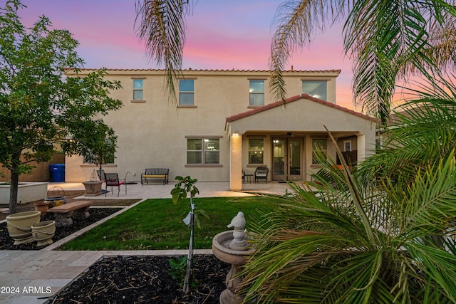 back house at dusk featuring a patio and a lawn