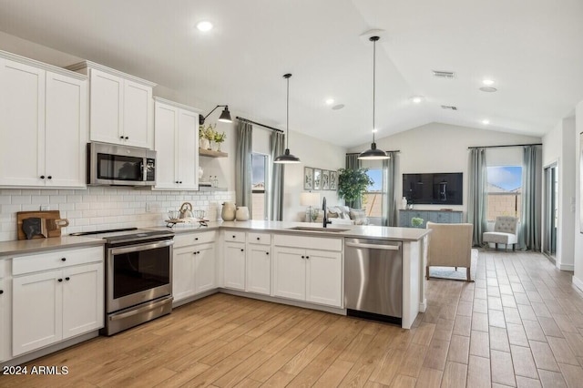 kitchen with vaulted ceiling, white cabinetry, hanging light fixtures, sink, and stainless steel appliances