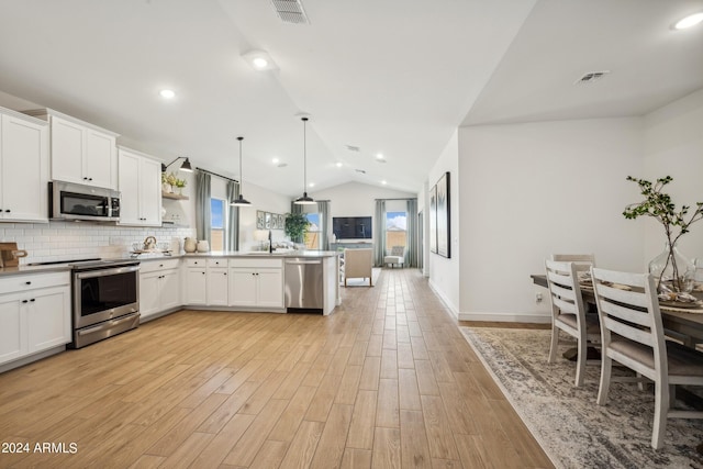 kitchen with white cabinets, lofted ceiling, stainless steel appliances, hanging light fixtures, and light wood-type flooring