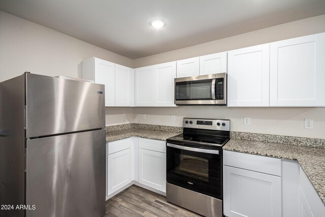 kitchen featuring white cabinetry, appliances with stainless steel finishes, light stone counters, and wood finished floors