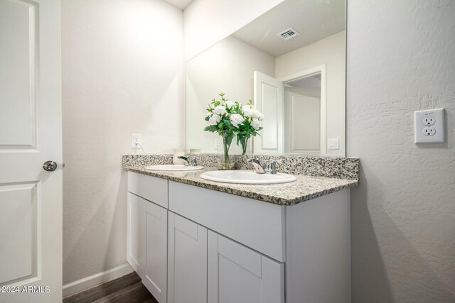 bathroom featuring a textured wall, visible vents, a sink, and double vanity