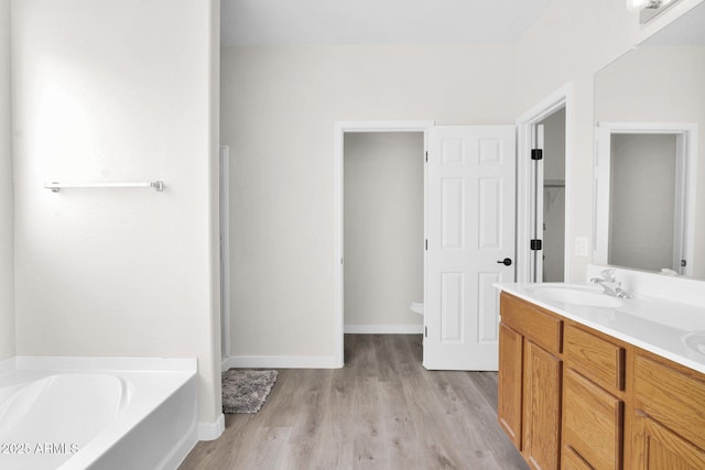 bathroom featuring wood-type flooring, a bath, vanity, and toilet