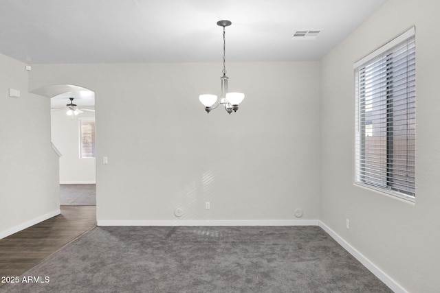 empty room with dark colored carpet, ceiling fan with notable chandelier, and a wealth of natural light