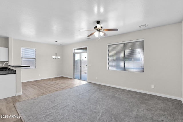 unfurnished living room with sink, ceiling fan with notable chandelier, plenty of natural light, and hardwood / wood-style floors