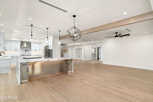 kitchen featuring a spacious island, white cabinetry, pendant lighting, and wall chimney range hood