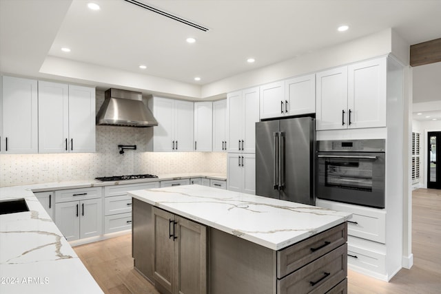 kitchen with white cabinetry, light stone counters, stainless steel appliances, and wall chimney exhaust hood