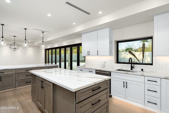 kitchen with sink, white cabinetry, a kitchen island, pendant lighting, and light stone countertops