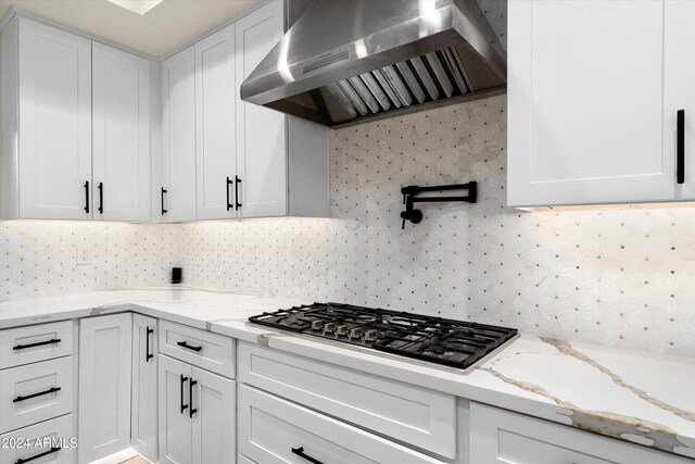 kitchen with white cabinets, decorative backsplash, stainless steel gas cooktop, light stone counters, and wall chimney range hood