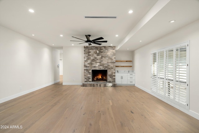 unfurnished living room featuring a fireplace, light hardwood / wood-style floors, and ceiling fan