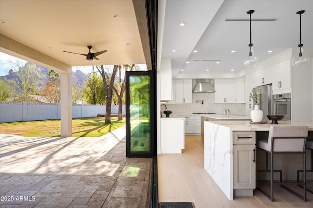 5919 N 45th St, Phoenix, AZ 85018 - kitchen featuring stainless steel appliances, wall chimney range hood, a ceiling fan, backsplash, and white cabinetry