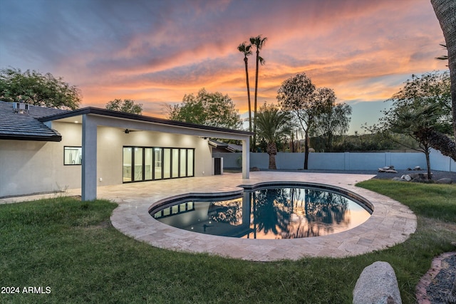 pool at dusk featuring a patio, ceiling fan, and a lawn