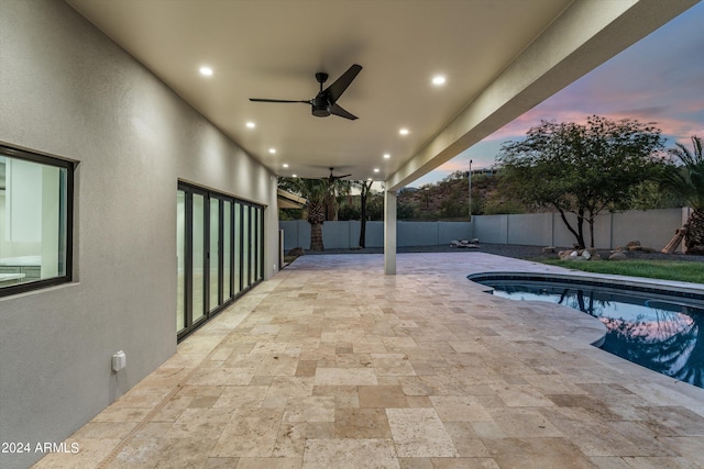 pool at dusk with ceiling fan and a patio