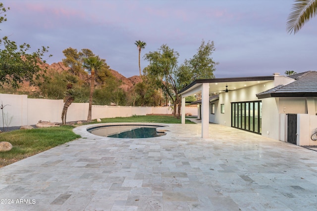 pool at dusk with ceiling fan and a patio