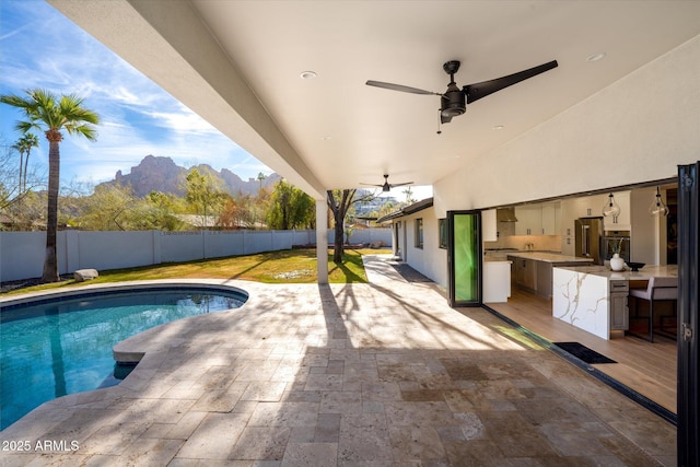 view of pool with ceiling fan, an outdoor kitchen, a mountain view, and a patio area