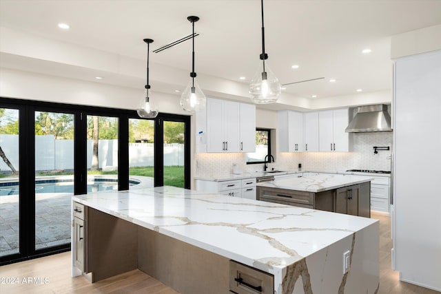 kitchen with decorative light fixtures, a spacious island, white cabinets, light stone counters, and wall chimney exhaust hood