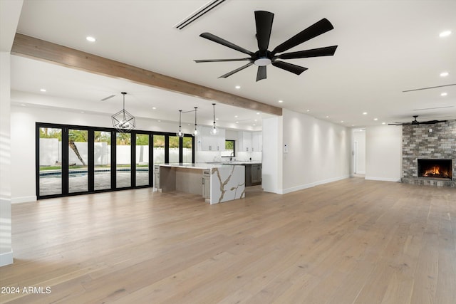 unfurnished living room featuring beam ceiling, a stone fireplace, light hardwood / wood-style floors, and ceiling fan