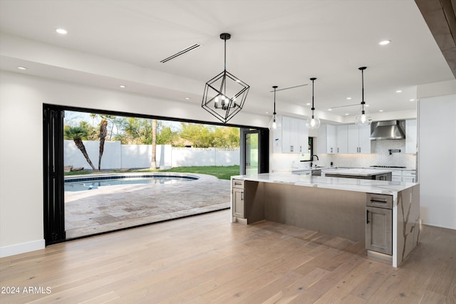 kitchen featuring pendant lighting, wall chimney range hood, white cabinets, and light stone counters