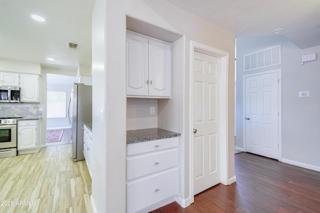 3921 W Jasper Dr, Chandler, AZ 85226 - kitchen with stainless steel appliances, white cabinets, light wood-type flooring, dark stone countertops, and baseboards