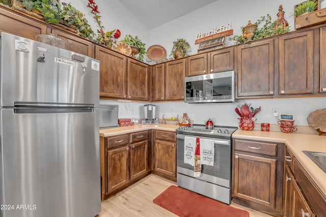 kitchen with stainless steel appliances, lofted ceiling, and light hardwood / wood-style floors