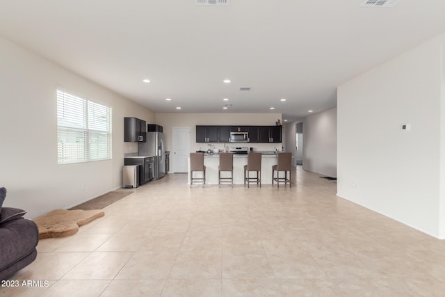 kitchen featuring light tile patterned flooring, appliances with stainless steel finishes, a kitchen island with sink, and a kitchen breakfast bar