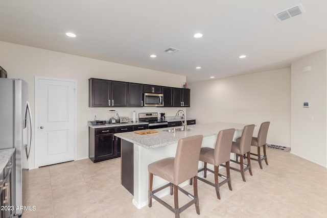 kitchen featuring sink, a breakfast bar area, appliances with stainless steel finishes, an island with sink, and light stone countertops