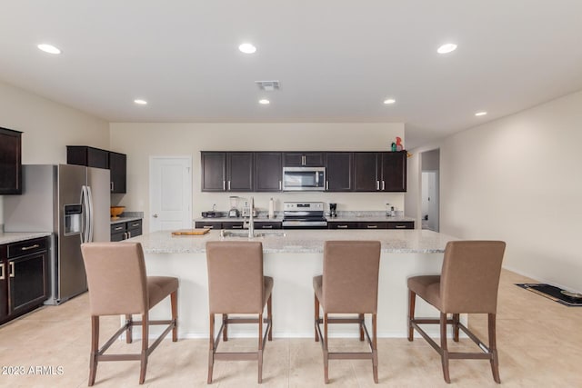 kitchen featuring a kitchen island with sink, sink, light stone counters, and appliances with stainless steel finishes