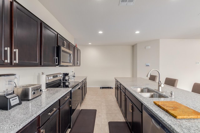 kitchen with appliances with stainless steel finishes, a breakfast bar, sink, light tile patterned floors, and light stone counters