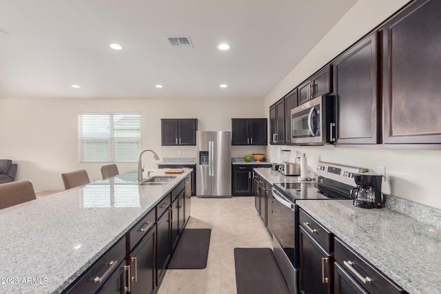 kitchen with a kitchen bar, sink, light tile patterned floors, stainless steel appliances, and light stone countertops