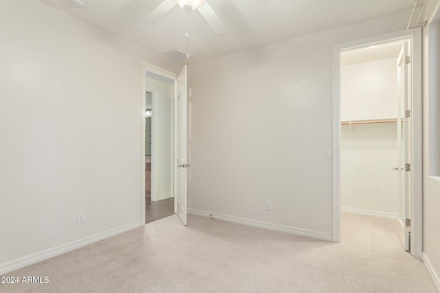 unfurnished bedroom featuring a spacious closet, a closet, ceiling fan, and light colored carpet