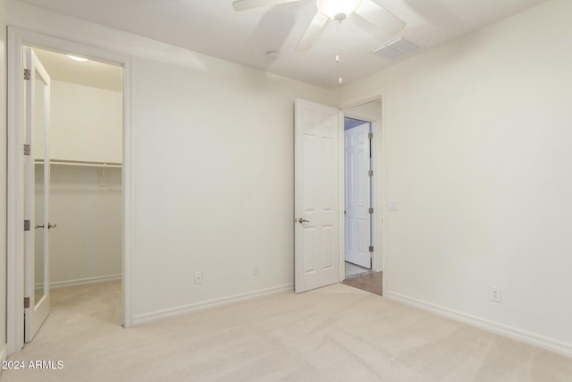 unfurnished bedroom featuring a walk in closet, ceiling fan, a closet, and light carpet