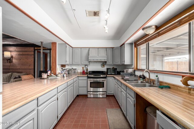 kitchen with sink, gray cabinetry, dark tile patterned flooring, stainless steel range, and custom range hood