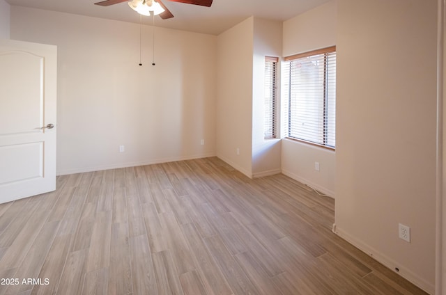 spare room featuring light wood finished floors, a ceiling fan, and baseboards