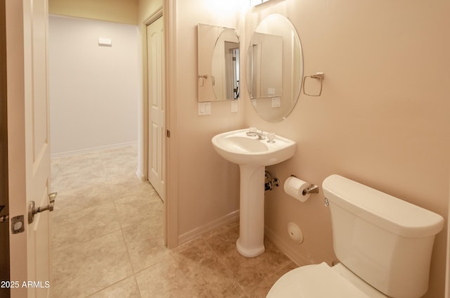 half bathroom featuring toilet, baseboards, a sink, and tile patterned floors