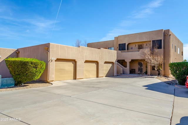 pueblo revival-style home featuring a garage, driveway, and stucco siding